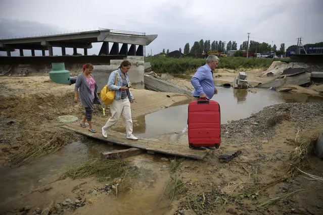 Tourists walk to an airport along a road damaged by floods near the village of Tsybanobalka, Krasnodar region, Russia, Saturday, August 14, 2021. (Photo by AP Photo/Stringer)