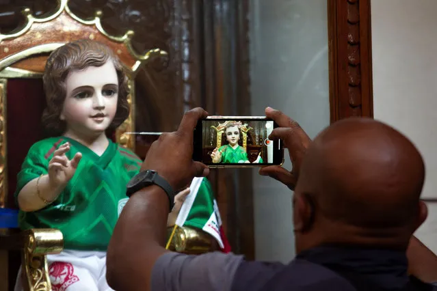 A man takes a picture of a doll representing the Child of the Miracles dressed in the Mexican national soccer team jersey at the Parroquia San Gabriel Arcangel a day before the match between Mexico and Poland during the FIFA World Cup Qatar 2022, in Mexico City, Mexico on November 21, 2022. (Photo by Quetzalli Nicte-Ha/Reuters)