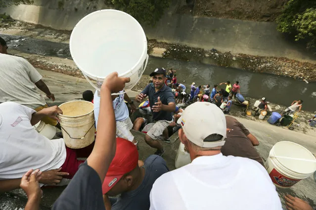 People collect water from a leaking pipeline above the Guaire River during rolling blackouts, which affects the water pumps in people's homes, offices and stores, in Caracas, Venezuela, Monday, March 11, 2019. The blackout has intensified the toxic political climate, with opposition leader Juan Guaido blaming alleged government corruption and mismanagement and President Nicolas Maduro accusing his U.S.-backed adversary of sabotaging the national grid. (Photo by Fernando Llano/AP Photo)