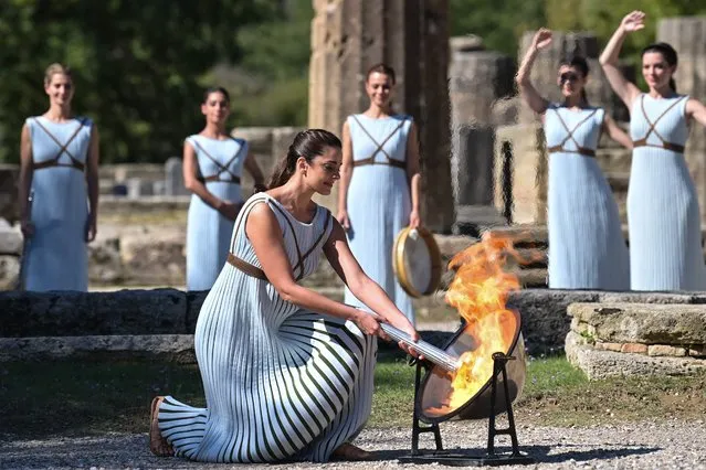 Greek actress Xanthi Georgiou, playing the role of the High Priestess, lights up the torch during the flame lighting ceremony for the Beijing 2022 Winter Olympics at the Ancient Olympia archeological site, birthplace of the ancient Olympics in southern Greece on October 18, 2021. The Olympic flame will once again be lit in an empty stadium on Ovtober 18, 2021, as it starts its truncated journey to Beijing for the Winter Games in February. Like the ceremony in March 2020 to light the flame for Tokyo, and like those Games, which were put back a year, Monday's ceremony is a victim of coronavirus restrictions. (Photo by Aris Messinis/AFP Photo)