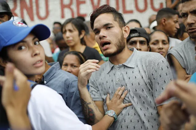 People wait to be given empty water containers and water purification pills during the Red Cross' first aid shipment in Caracas, Venezuela, Tuesday, April 16, 2019. In late March, the Red Cross federation announced it would soon begin delivering assistance to an estimated 650,000 people and vowed that it would not accept interference from either side of the polarized country. (Photo by Ariana Cubillos/AP Photo)