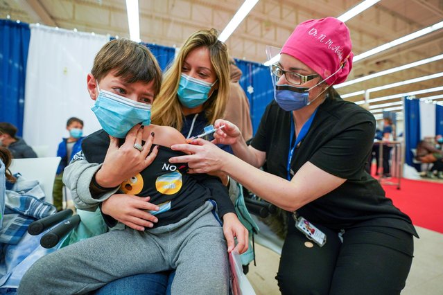 Dean Eliaz is comforted by his mom Michelle Eliaz as he gets his shot at a Humber River Hospital vaccination clinic after Canada approved Pfizer's coronavirus disease (COVID-19) vaccine for children aged 5 to 11, in Toronto, Ontario, Canada on November 25, 2021. (Photo by Carlos Osorio/Reuters)