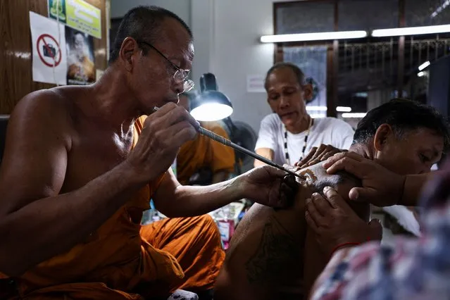 A Buddhist monk uses a traditional needle to tattoo the body of a man during a religious tattoo festival at Wat Bang Phra monastery in Nakhon Pathom province, Thailand, on March 23, 2024.  Devotees were seen running, growling, shouting, and gesticulating wildly throughout the temple grounds. The sacred images covering their bodies are believed to offer protection, bring good luck, and even heal sickness to those who receive them. (Photo by Chalinee Thirasupa/Reuters)