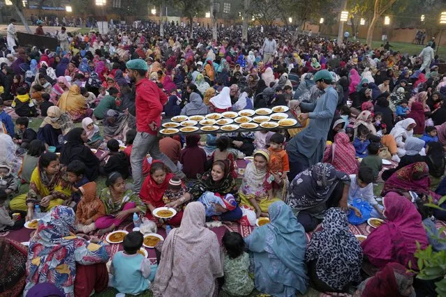 Volunteers serve meals among families for breaking their fast during the Muslim's holy fasting month of Ramadan, at a free meal distribution point run by a charity group, in Lahore, Pakistan, Wednesday, March 13, 2024. (Photo by K.M. Chaudary/AP Photo)