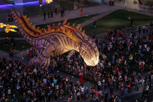 People look at the inflatable dinosaur of “Saurian and the Witnesses of Outer Space” -the night parade of the French Plasticiens Volants company- during the inauguration of the “Teatro a Mil” international festival, in front of La Moneda Presidential Palace in Santiago, on January 3, 2023. (Photo by Javier Torres/AFP Photo)