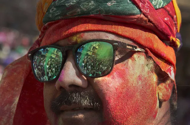 Indians dancing during the Holi celebrations are reflected on the sun glass of a man who has his face smeared in colors in Gauhati, India, Monday, March 13, 2017. The festival also heralds the arrival or spring. (Photo by Anupam Nath/AP Photo)