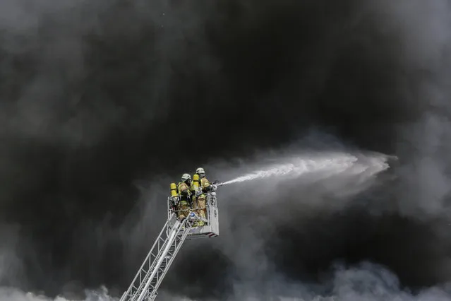 Fire fighters spray water in front of smoke at a burning storage hall of the Dong Xuan Center, an Asia market specialized in Vietnamese goods, in Berlin, Germany, Wednesday, May 11, 2016. The fire department sent some 150 trucks and other vehicles to the fire which broke out Wednesday morning. (Photo by Markus Schreiber/AP Photo)