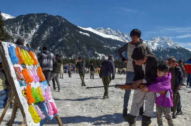 Children pop balloons with air-gun before the start of the Winter Snow Sports Festival in Kalam, about 99 km from Mingora in the northern upper reaches of Swat valley on February 12, 2022. (Photo by Abdul Majeed/AFP Photo)