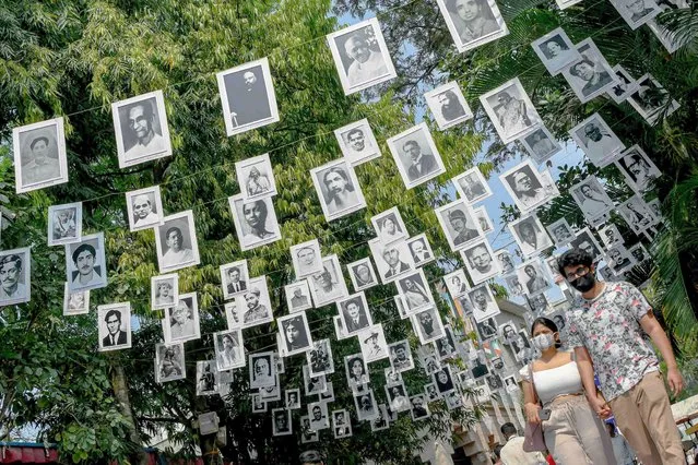 Visitors pass under buntings displaying portraits of famous personalities during the annual “Chitra Santhe” – Art Carnival, a daylong annual fest organised by Chitrakala Parishath, for artists to showcase and sell their art work, in Bangalore on March 27, 2022. (Photo by Manjunath Kiran/AFP Photo)