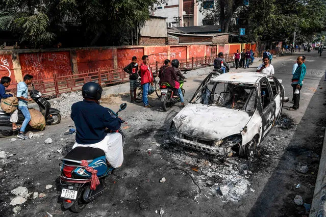 Commuters drive past the remains of gutted vehicles on a road in Guwahati on December 13, 2019, a day after protests against the government's Citizenship Amendment Bill (CAB) broke out across India's northeastern state of Assam. Internet access has been cut in India's northeastern city of Guwahati after violent protests over a new citizenship law saw two demonstrators shot dead by police, authorities said on December 13. (Photo by Sajjad Hussain/AFP Photo)
