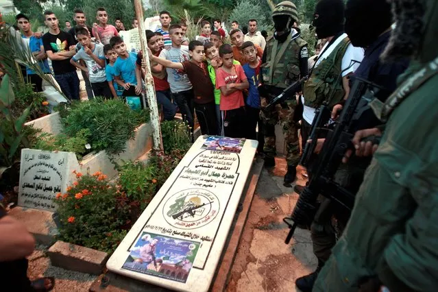 Palestinian youths watch as masked militants pray at the grave of Hamza Abu el-Heija, a comrade who was recently killed in clashes with Israeli troops, in the Jenin refugee camp, West Bank Monday, July 28, 2014. Monday marked the beginning of the three-day Eid al-Fitr holiday, which caps the Muslim fasting month of Ramadan. (Photo by Mohammed Ballas/AP Photo)