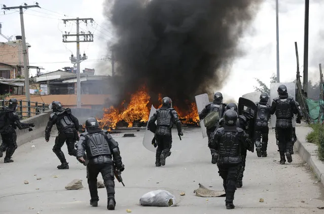 Police run toward a flaming barricade set by striking truckers in Bogota, Colombia, Wednesday, July 20, 2016. Hundreds of truckers clashed with police on Wednesday on the 41st day of their strike which has made food scarce in some areas of the country. Truckers are demanding a higher price for freight, lower fuel prices and fewer license regulations for cargo. (Photo by Fernando Vergara/AP Photo)