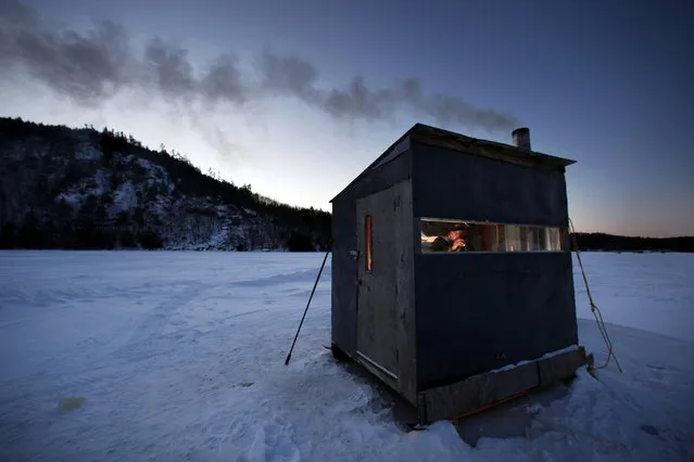 Tom Locklin, of Bethel, Maine, sips a beer as he looks out of his warm ice fishing shack on Christopher Lake where the temperature was 0 degrees at dusk, Thursday, January 15, 2009, in Bryant Pond, Maine. (Photo by Robert F. Bukaty/AP Photo)