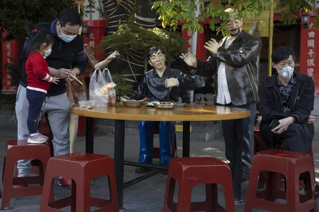 Residents wearing masks to help curb the spread the coronavirus rest among statues depicting normal life along a retail street in Wuhan, central China's Hubei province, Thursday, April 9, 2020. (Photo by Ng Han Guan/AP Photo)