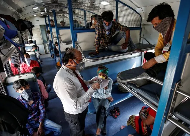 A railway official takes the details of migrant workers sitting inside a train, who were stranded in Gujarat due to a lockdown imposed by the government to prevent the spread of the coronavirus disease (COVID-19), as they leave for their home state of Uttar Pradesh, in Ahmedabad, India, May 2, 2020. (Photo by Amit Dave/Reuters)