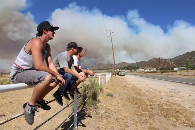 Kris Ensz, Jacob Maidment and Kirkland Brown hang out across from Kirkland's parents home in Summit Valley, Calif., east of Silverwood Lake on Sunday, August 7, 2016. With a wildfire burning nearby, they helped Kirkland's dad, Brian, ready the home by hosing things down and moving vehicles and valuables. Firefighters are battling a wildfire in Southern California that grew to more than 2 square miles in mere hours and forced the evacuation of homes near a reservoir. The fire, which broke out Sunday afternoon in the San Bernardino National Forest, prompted the evacuation order of the sparsely populated Summit Valley area east of the dam. (Photo by John M. Blodgett/The Inland Valley Daily Bulletin via AP Photo)