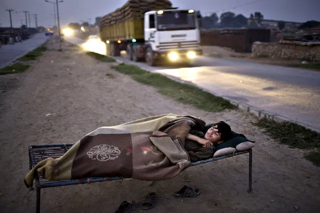 A Pakistani youth, who was Internally Displaced from Pakistan's tribal areas, sleeps on a bed to escape the heat trapped in his mud home, near a wholesale fruit and vegetable market where he works, on the outskirts of Islamabad, Pakistan, early Monday, September 22, 2014. (Photo by Muhammed Muheisen/AP Photo)