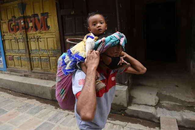 A construction worker carries a cooking gas cylinder with his baby on his shoulders as he makes his way through a closed market during a government-imposed nationwide lockdown as a preventive measure against the COVID-19 coronavirus, in Kathmandu on May 29, 2020. (Photo by Prakash Mathema/AFP Photo)