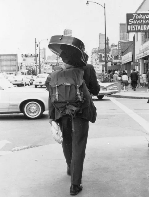 In this October 16, 1967, file photo, a man carries a guitar, a loaf of bread and a knapsack as he walks down the street away from the Haight-Ashbury district of San Francisco. (Photo by AP Photo)