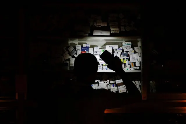 A salesman of a pharmaceutical shop uses his cellphone torch to find medicine to serve customers during a countrywide blackout in Dhaka, Bangladesh on October 4, 2022. (Photo by Mohammad Ponir Hossain/Reuters)