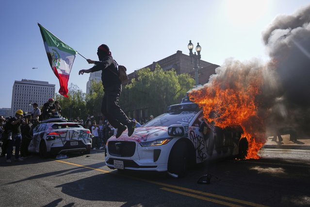 A protester leaps off a burning Waymo taxi near the metropolitan detention center of downtown Los Angeles, Sunday, June 8, 2025, following last night's immigration raid protest. (Photo by Eric Thayer/AP Photo)