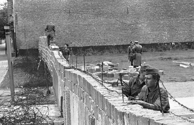 The September 9, 1961 file photo shows East-German policemen in work dress as they remove barbed wire from a brick wall while other policemen in background are raising the wall to 15 feet at the border between the French and Russian sector at Bernauer Strasse in Berlin. (Photo by Edwin Reichert/AP Photo)