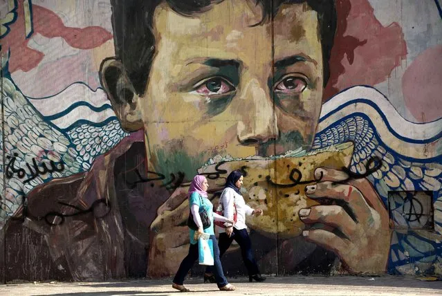 Egyptians walk in front of a mural related to the January 25, 2011 revolution, near Tahrir Square in Cairo, Egypt, Wednesday, August 10, 2016. Three Egyptian dailies said that Cairo was proposing to IMF delegates an 18-month reform program in return for a $12 billion loan over three years to shore up its economy, but that differences remained between the two sides on how to proceed. (Photo by Amr Nabil/AP Photo)