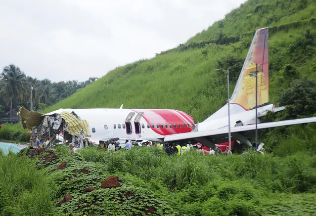 Officials stand on the debris of the Air India Express flight that skidded off a runway while landing in Kozhikode, Kerala state, India, Saturday, August 8, 2020. The special evacuation flight bringing people home to India who had been trapped abroad because of the coronavirus skidded off the runway and split in two while landing in heavy rain killing more than a dozen people and injuring dozens more. (Photo by C.K.Thanseer/AP Photo)