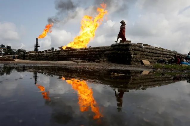A reflection of two gas flaring furnaces and a woman walking on sand barriers is seen in the pool of oil-smeared water at a flow station in Ughelli, Delta State, Nigeria on September 17, 2020. (Photo by Afolabi Sotunde/Reuters)