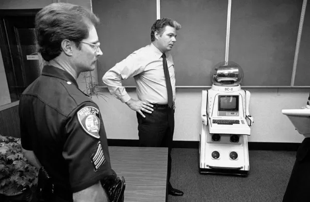 Sgt. Tom Van Ansdell of the Beverly Hills, Calif., police department displays a 4-foot robot at police station in Beverly Hills on August 18, 1982. The robot, complete with color television screen and camera, micro computer and two-day communications, was taken into police custody after it was found clanking through Beverly Hills during Tuesday rush hour. Police took the robot into custody when the person, as yet unidentified, operating it by remote control, refused to identify himself to police. (Photo by Lennox McLendon/AP Photo)