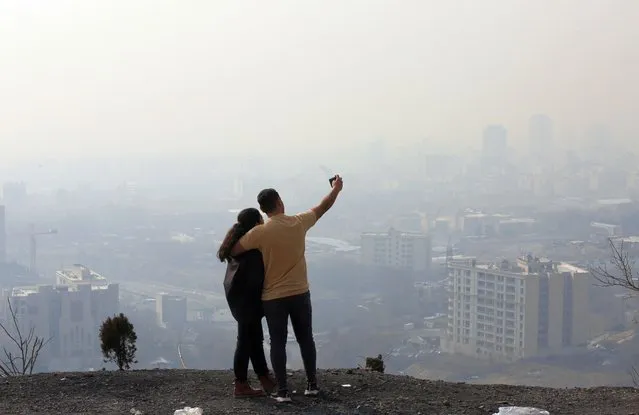 An Iranian couple takes a selfie as smog obscures the skyline in Tehran, Iran, 02 January 2023. According to the Iranian meteorology organization the country's capital Tehran is in a red warning zone, prompting the Iranian government to announce a closure of schools and universities for two days while implementing stricter rules for traffic zones and insisting that elderly and sick people stay indoors. (Photo by Abedin Taherkenareh/EPA/EFE)