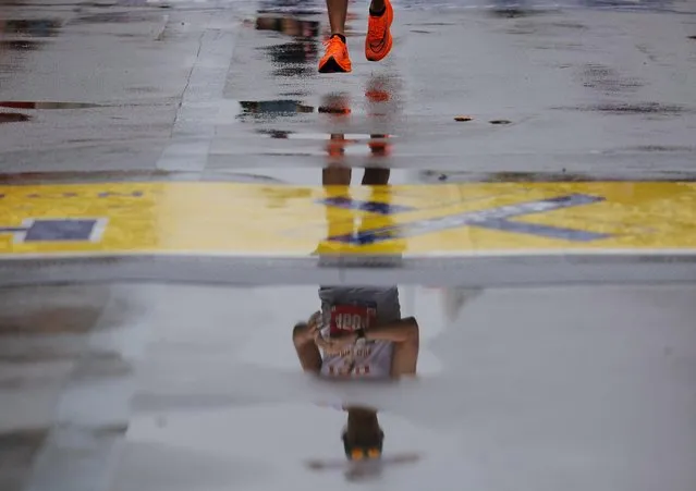 A participant is seen in the reflection of a puddle as they cross finish line of the the 127th Boston Marathon in Boston, Massachusetts, U.S. on April 17, 2023. (Photo by Brian Snyder/Reuters)