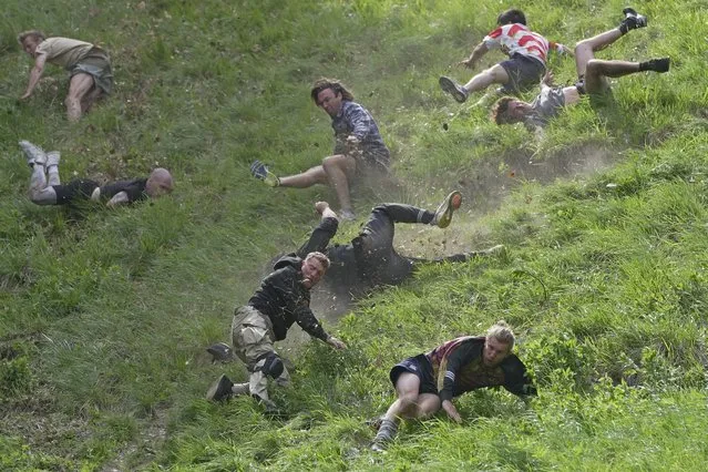 Participants compete in the men's downhill race during the Cheese Rolling contest at Cooper's Hill in Brockworth, Gloucestershire on Monday May 29, 2023. The Cooper's Hill Cheese-Rolling and Wake is an annual event where participants race down the 200-yard (180 m) long hill chasing a wheel of double gloucester cheese. (Photo by Kin Cheung/AP Photo)