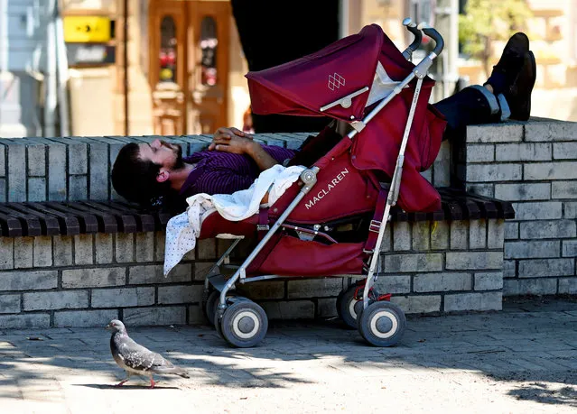 A man and his baby sleep in the shadow in the center of Kiev, Ukraine during a hot summer day on June 4, 2018. (Photo by Sergei Supinsky/AFP Photo)