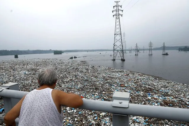 A person looks at a huge pile of garbage on a flooded river after remnants of Typhoon Doksuri brought rains and floods in Beijing, China on August 2, 2023. (Photo by Tingshu Wang/Reuters)