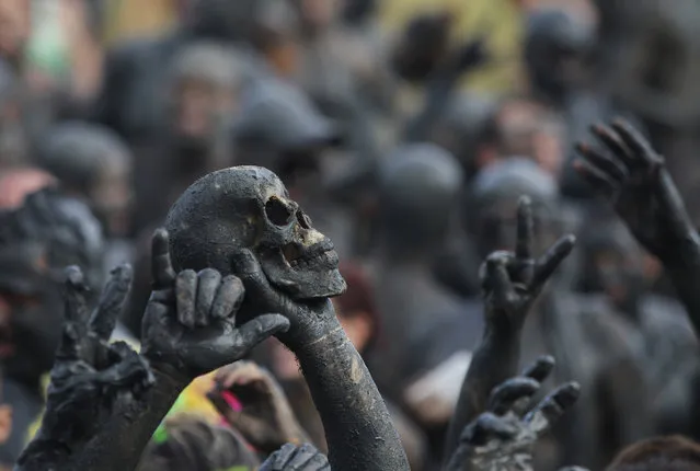 A man holds up a skull during the traditional “Bloco da Lama” or “Mud Block” carnival party, in Paraty, Brazil, Saturday, February 14, 2015. (Photo by Leo Correa/AP Photo)