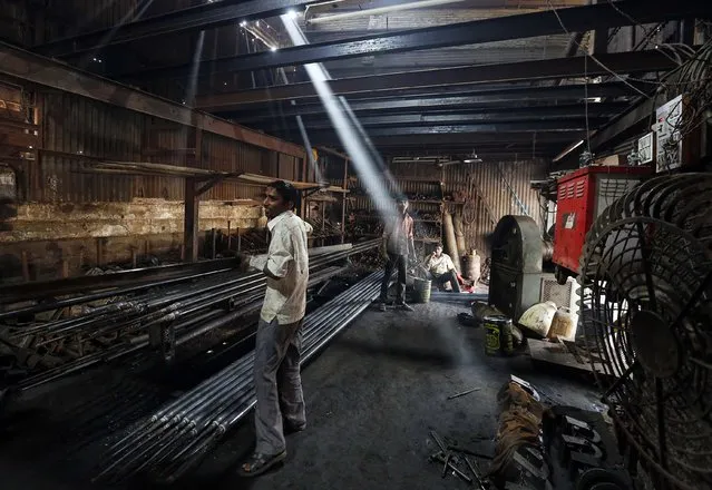 A worker carries an iron pipe inside a metal fabrication workshop in an industrial area of Mumbai February 9, 2015. (Photo by Shailesh Andrade/Reuters)
