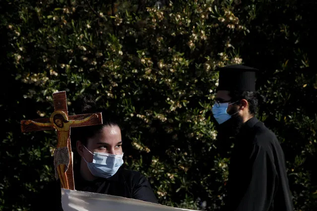 A female protestor holds a cross as an Orthodox priest passes during a protest against the Cyprus' song in Eurovision, outside Cyprus' national broadcasting building in capital Nicosia, Cyprus, Wednesday, May 19, 2021. Several dozen Orthodox Christian faithful including clergymen held up wooden crucifixes, icons of saints and a banner declaring Cyprus’ love for Christ in a renewed protest over Cyprus’ controversial entry for the Eurovision song contest that they contend promotes worship of Satan. (Photo by Petros Karadjias/AP Photo)