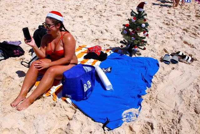 Irish backpacker Genna Woods talks to relatives on her phone as she sits next to her small Christmas tree she planted in the sand as she celebrates Christmas Day at Sydney's Bondi Beach in Australia, December 25, 2016. (Photo by David Gray/Reuters)