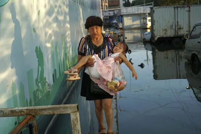 A woman carries a child in her arms as she walks on a curb above floodwaters in Xinxiang in central China's Henan Province, Monday, July 26, 2021. Record rain in Xinxiang last week left the produce and seafood market soaked in water. Dozens of people died in the floods that immersed large swaths of central China's Henan province in water. (Photo by Dake Kang/AP Photo)