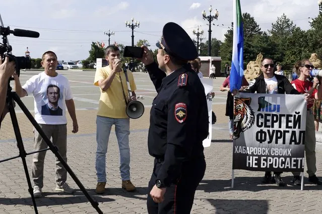 A police officer looks at a group of demonstrators in Khabarovsk, Russia, who had gathered in support of Sergei Furgal, the former governor of the region in the country's Far East, on Saturday, September 11, 2021. A few demonstrators gather in a persistent reminder of the larger protests last year demanding the release of the region's former governor, Sergei Furgal. (Photo by Sergei Demidov/AP Photo)