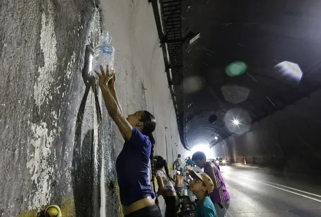 A woman collects water from a spout in a highway tunnel, in Caracas, Venezuela, Monday, April 1, 2019. (Photo by Ariana Cubillos/AP Photo)