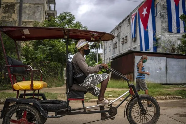 A bicycle taxi passes the home of Yunior Garcia Aguilera, one of the organizers of a banned opposition march, draped with Cuban flags as a way to block his windows and prevent his communicating with the outside in Havana, Cuba, Monday, November 15, 2021. Cuban authorities consider García's group Archipiélago, an internet debate forum, illegal. (Photo by Ramon Espinosa/AP Photo)