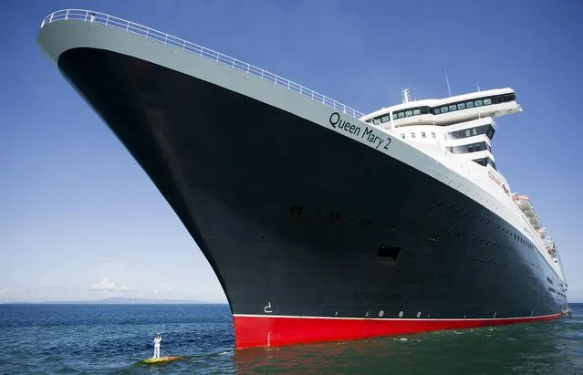 Captain Kevin Oprey (bottom L) standing beneath the soaring hull of Cunard's flagship Queen Mary 2, on March 6, 2014. (Photo by James Morgan/AFP Photo)