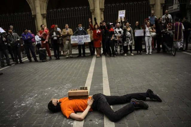 A man lies on the street covered with bricks on his back, during a performance against corruption,  in Pamplona, northern Spain, Thursday, May 14, 2015, prior to the Regional Spanish Elections to be held on May 24. (Photo by /Alvaro Barrientos/AP Photo)