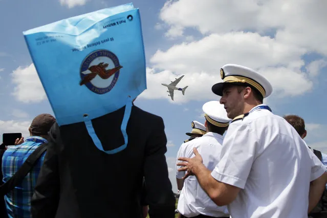 The Airbus A380 performs a demonstration flight as onlookers , one of them wearing a bag as a sun hat, at the Paris Air Show, in Le Bourget airport, north of Paris, Tuesday, June 16, 2015. Some 300,000 aviation professionals and spectators are expected at this weekends Paris Air Show, coming from around the world to make business deals and see dramatic displays of aeronautic prowess and the latest air and space technology. (AP Photo/Francois Mori)