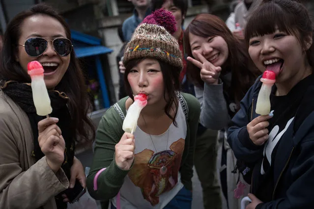 People pose for a photo as they eat phallic-shaped candy lollipops during Kanamara Matsuri (Festival of the Steel Phallus) on April 6, 2014 in Kawasaki, Japan. The Kanamara Festival is held annually on the first Sunday of April. The pen*s is the central theme of the festival, focused at the local pen*s-venerating shrine which was once frequented by prostitutes who came to pray for business prosperity and protection against sexually transmitted diseases. (Photo by Chris McGrath/Getty Images)