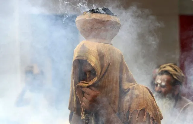 A Sadhu or a Hindu holy man covers his face as an earthen pot with burning “Upale” (or dried cow dung cakes) rests on his head during a prayer ceremony at the Simhastha Kumbh Mela in Ujjain, India, May 2, 2016. (Photo by Jitendra Prakash/Reuters)