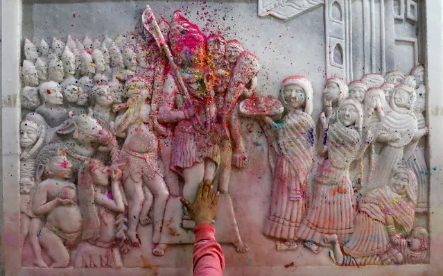 A man puts coloured powder on religious murals while praying inside the premises of a temple during Holi celebrations, in the old quarters of Delhi, India, March 18, 2022. (Photo by Anushree Fadnavis/Reuters)