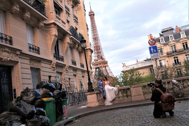 Newlyweds Fabiana, 44, and Rob Burns, 53, from the U.S., pose for a photographer in front of overflowing garbage bins in a street near the Eiffel Tower as garbage has not been collected due to a strike of garbage collectors against the French government pension reform, in Paris, France on March 27, 2023. (Photo by Nacho Doce/Reuters)